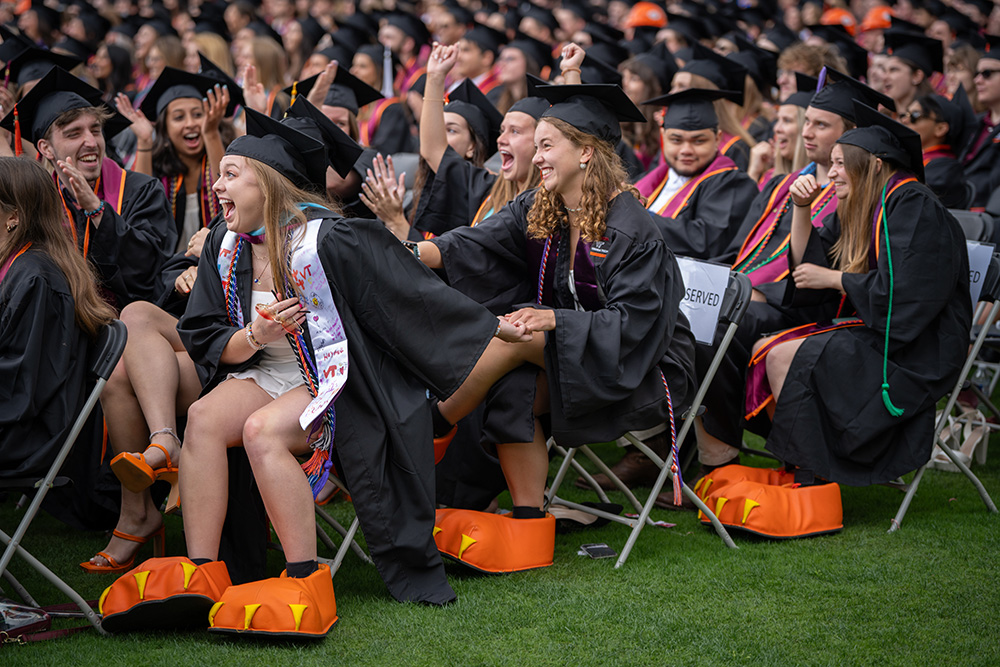 Three people react as they are announced as the HokieBird mascot during commencement