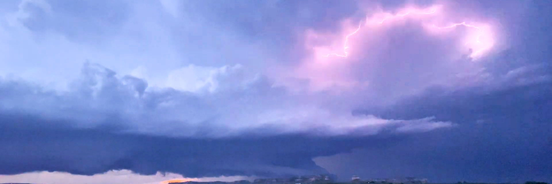 A large storm system dominates the landscape with an arc of lightning in the clouds