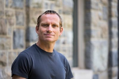 Robert Weiss poses in a t-shirt in front of a  Hokie Stone building. 