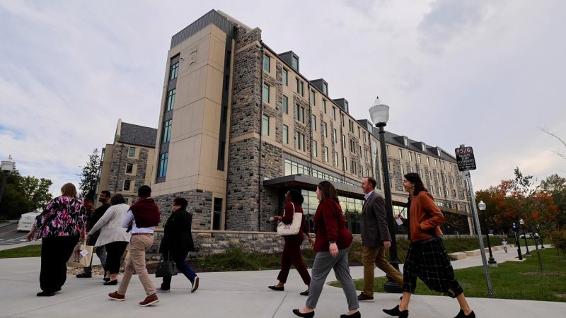 People walk past the five-story Creativity and Innovation District Building, clad in gray Hokie Stone and tan stucco 