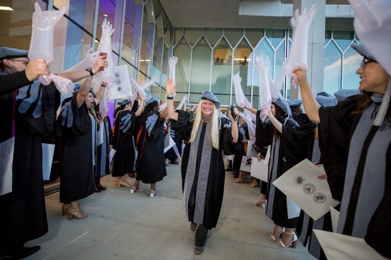 Jacquelyn Pelzer walking through a hall of graduates holding blown up gloves.
