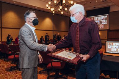Mike Mulhare receives a certificate of appreciation from President Tim Sands, shaking his hand.