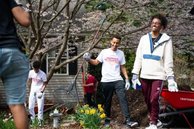 Students smile and laugh while doing yard work.