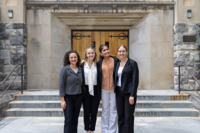 Four students smile and stand together outside of Pamplin Hall